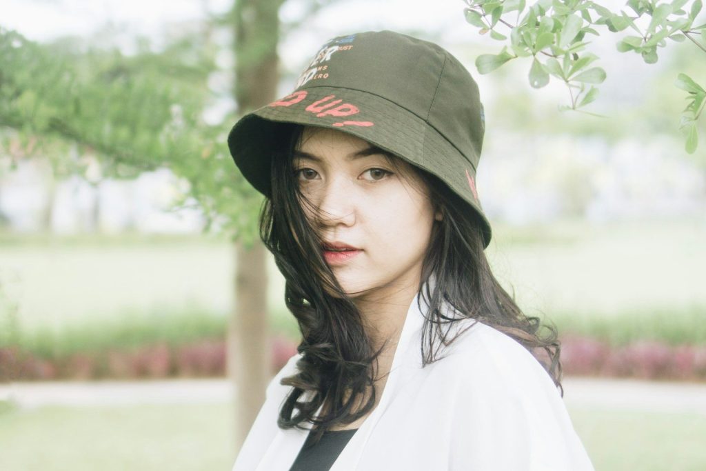 a woman wearing a hat standing under a tree