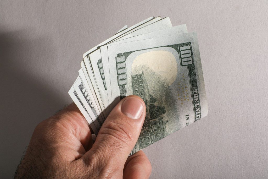 A hand holding a fan of us hundred dollar bills