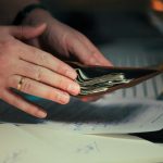 Hands holding cash in a wallet over papers.