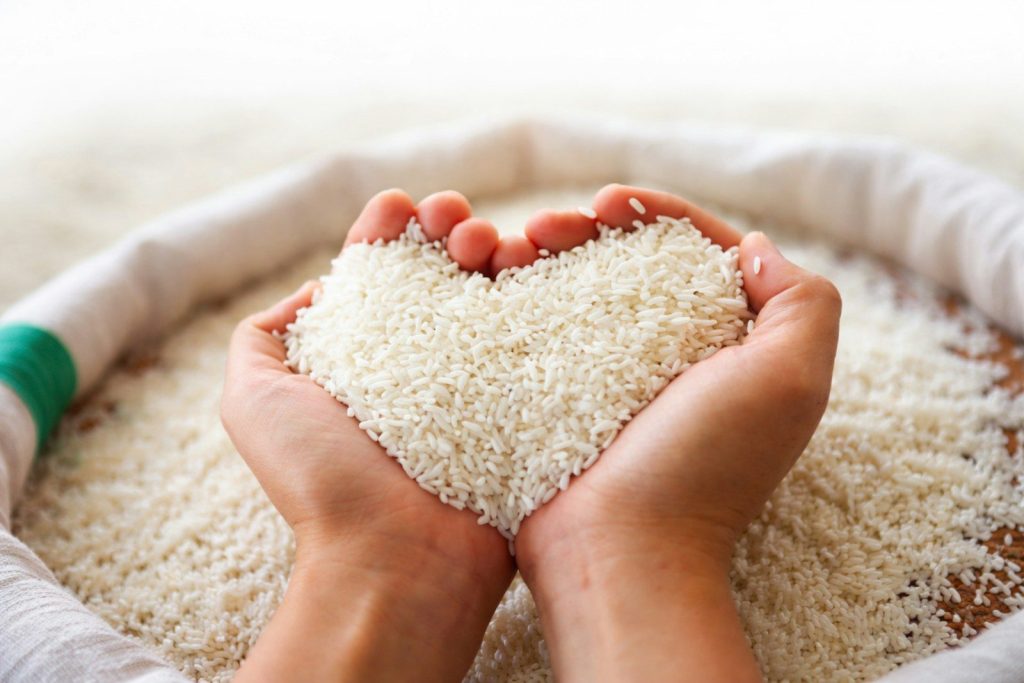 Hands forming a heart shape with white rice grains.