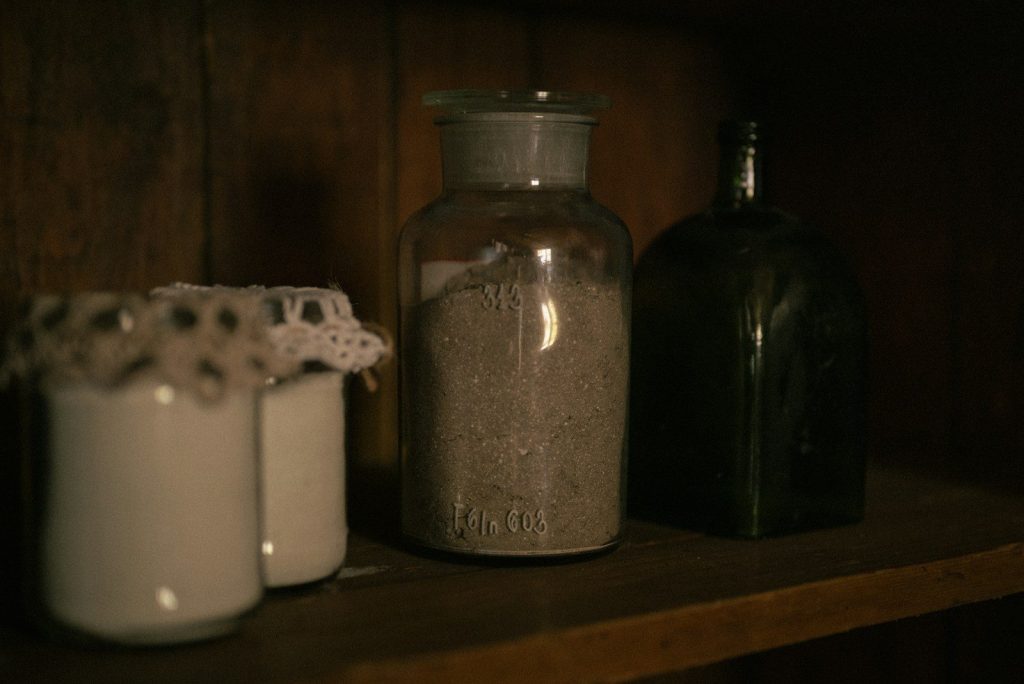 Old jars and bottles on a dark wooden shelf.
