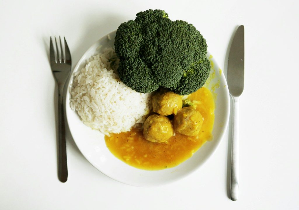 A plate of rice, broccoli, and meatballs with cutlery.