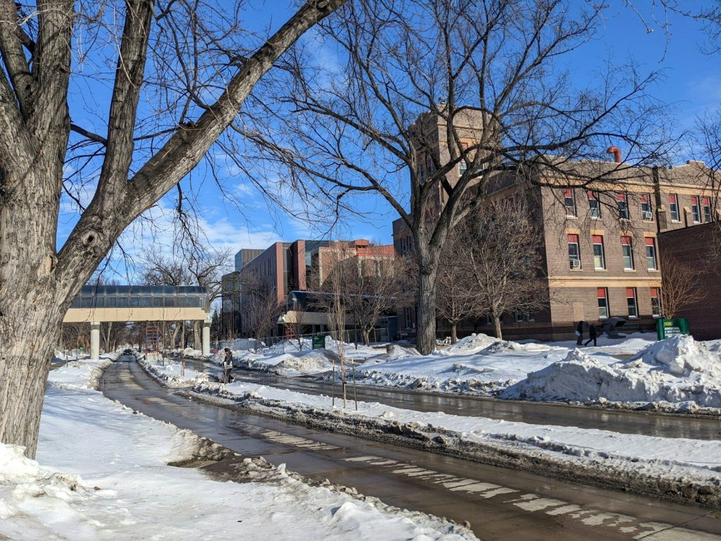 a city street with snow on the ground and buildings in the background