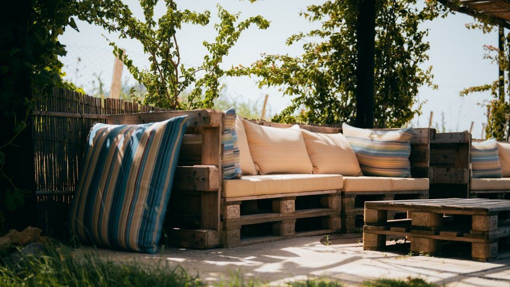 Rustic outdoor patio with pallet sofa and cushions under trees.