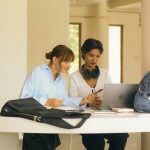 Two women studying together at a table with laptop.