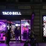 A purple lit store front with people walking by