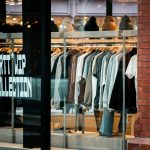 Clothes displayed on racks inside a store window.