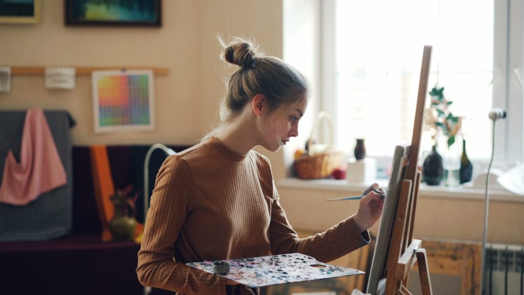 A woman paints on a canvas at her easel.