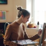 A woman paints on a canvas at her easel.