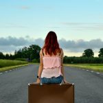 Red-haired woman sits on suitcase on empty road.
