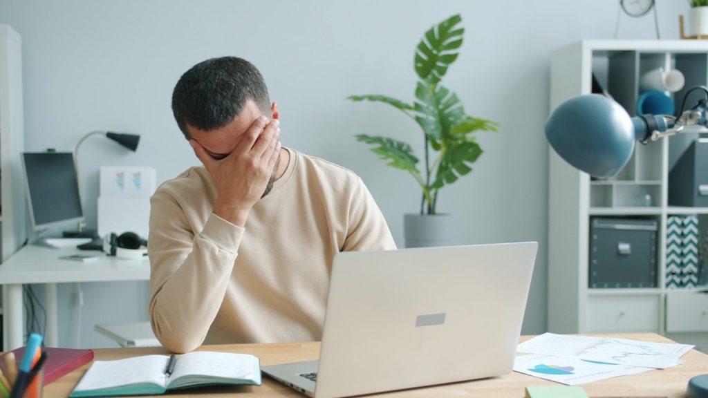 Man rubbing his face in front of laptop.