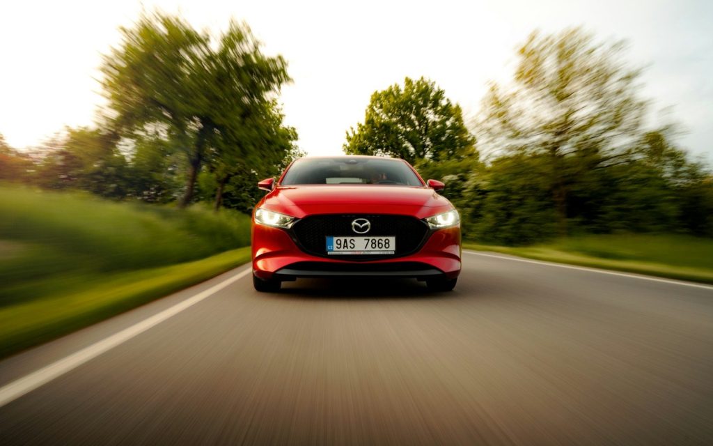 a red car driving down a road with trees in the background