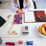 a woman sitting at a table with a plate of fruit and a calculator