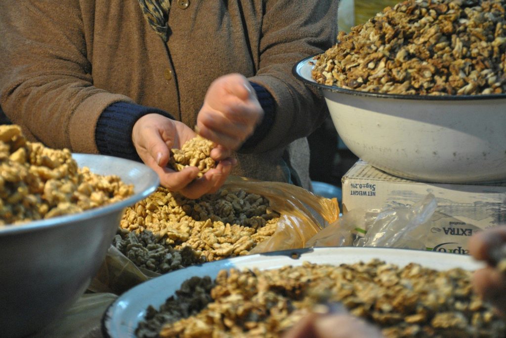 Hands sorting and packaging shelled walnuts from large bowls.