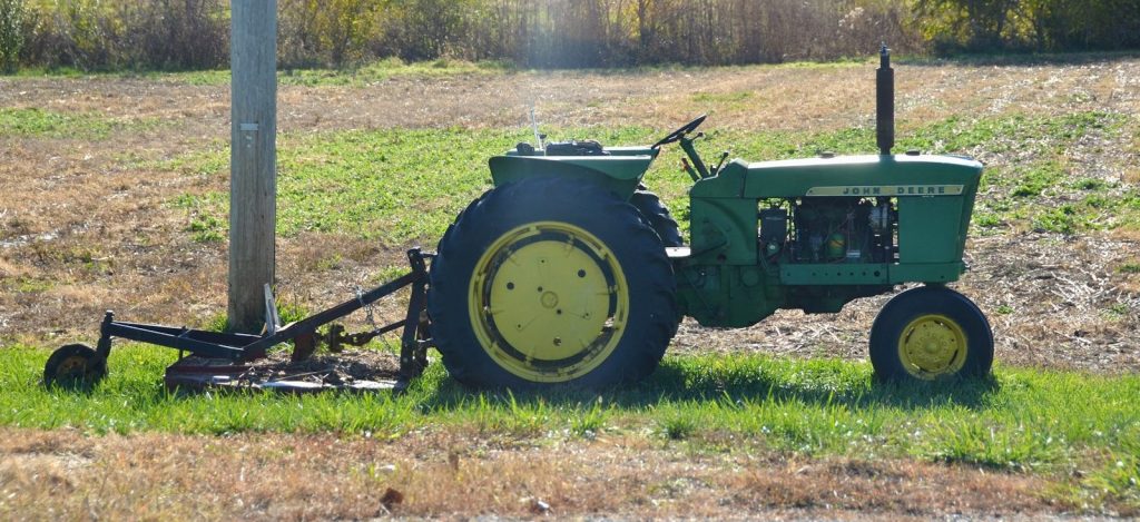 Green tractor with attached mower in grassy field.