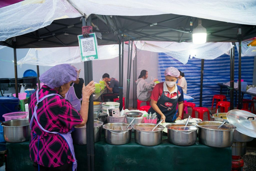 People working at a food stall with many pots.