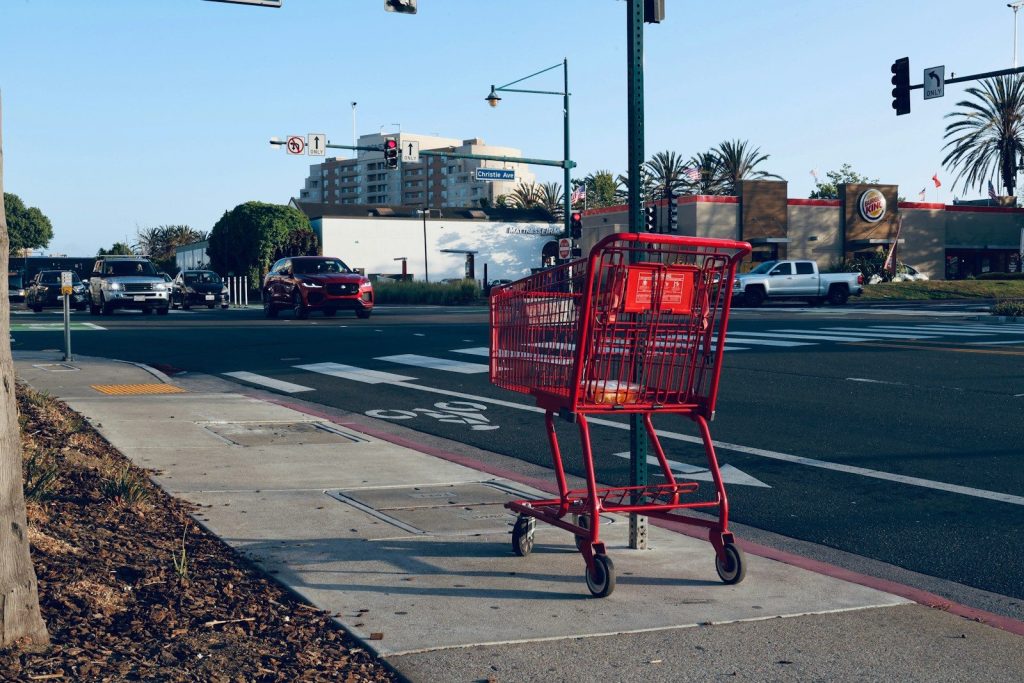 Red shopping cart on sidewalk near street.