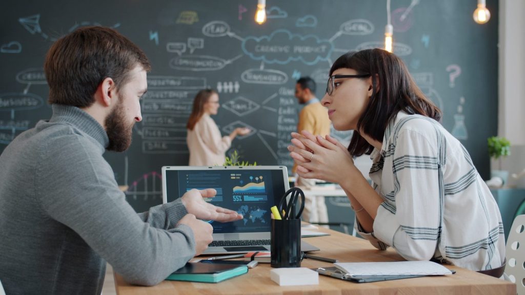 Two colleagues discussing charts on a laptop screen.