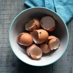 brown eggshells in round white ceramic bowl on gray wooden board top-view photography