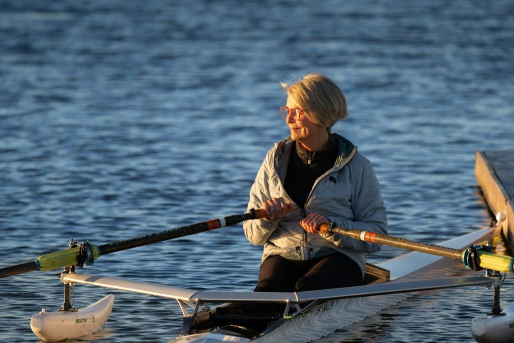 A woman rows her boat on calm water.