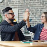 a man and a woman sitting at a table high fiving each other