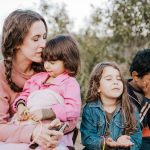 woman in blue denim jacket carrying girl in pink jacket during daytime