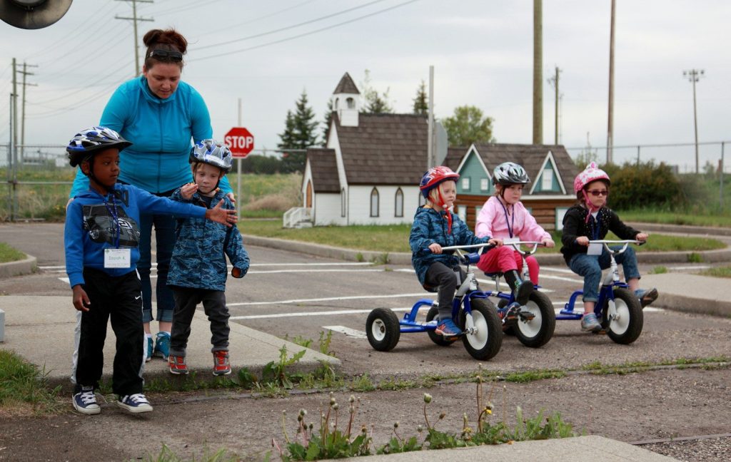 Children learn road safety on tricycles in a miniature town.
