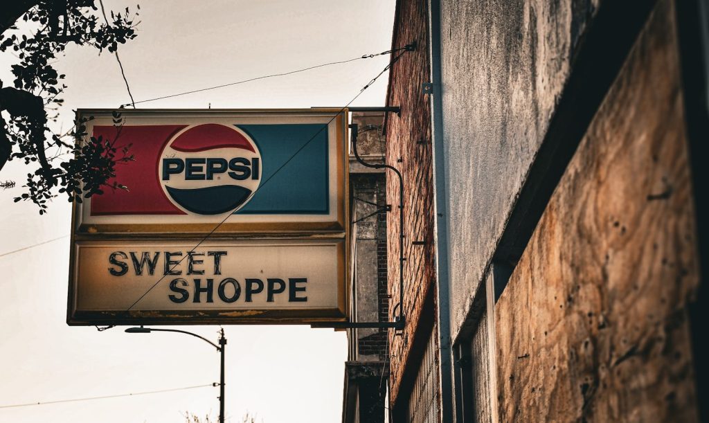 Old pepsi sign above a sweet shoppe storefront.
