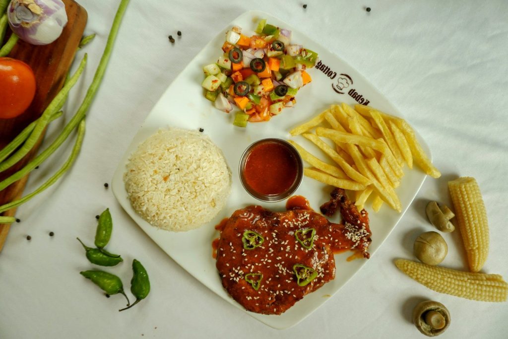 A meal with chicken, rice, fries, salad, and sauce.