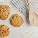 three oatmeal cookies next to a cooling rack and a wooden spoon