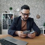 a man sitting at a table with a laptop and money