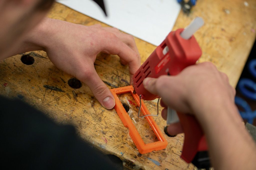 Hands using a hot glue gun on an orange object.