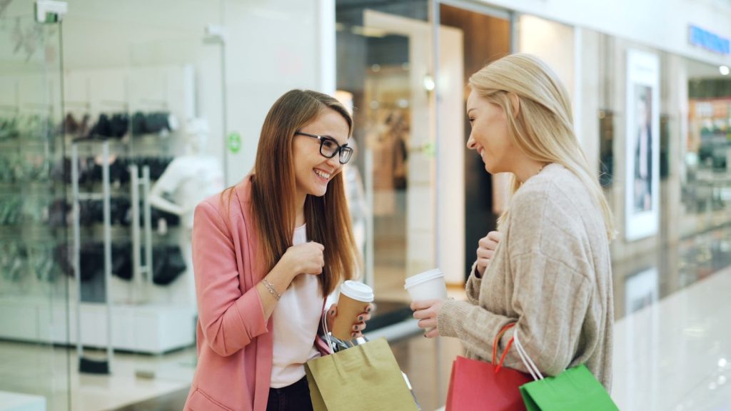 Two women with coffee cups talking in a mall.