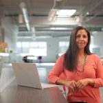 woman in orange long sleeve shirt sitting beside table with macbook pro