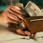 Hands holding us dollar bills in a brown leather wallet