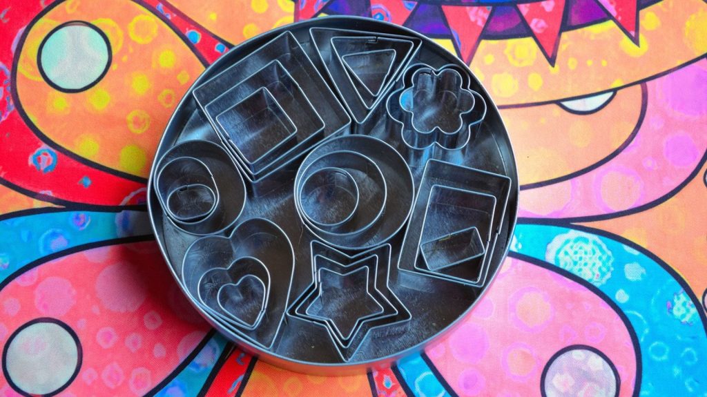Assorted metal cookie cutters in a circular tin.