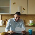 Man reading a letter at a kitchen table.