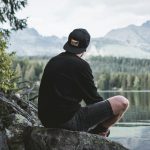 selective focus photography of man sitting on rock while looking at mountains
