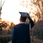 Graduating student celebrates on a path at sunset.
