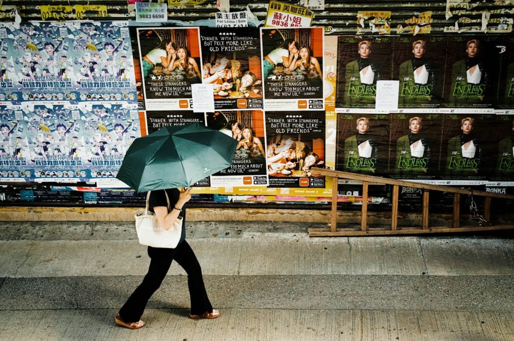 Person with umbrella walks past posters on wall.