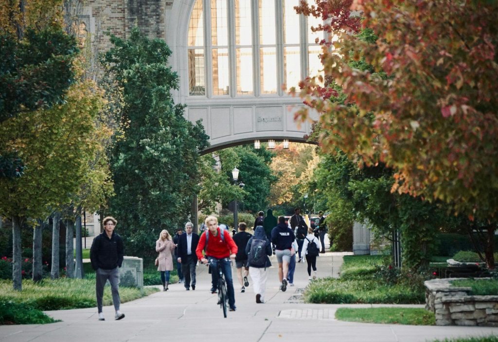 Students walk and bike on a college campus path.