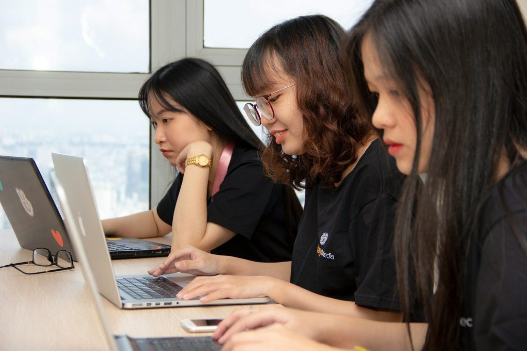three women sitting beside laptop computers close-up photography