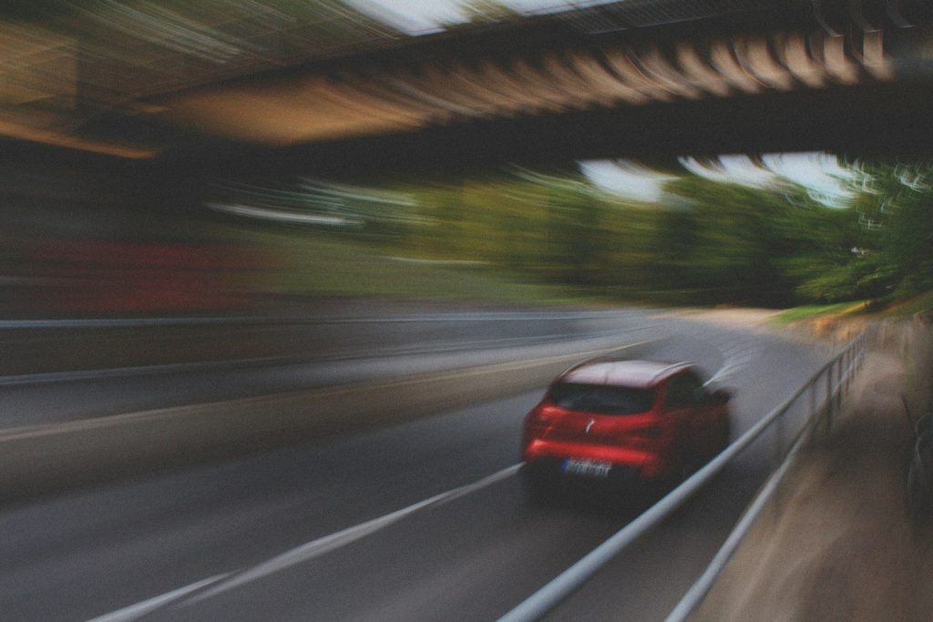 a red car driving down a street next to a bridge
