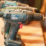 A row of cordless power drills on a wooden workbench, ready for use.