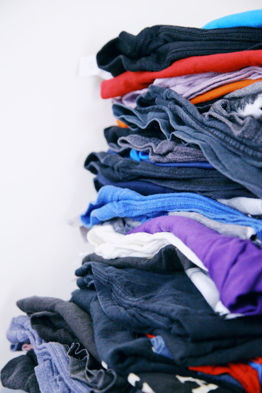 A neatly stacked pile of various colored clothes on a white surface, showcasing organization.