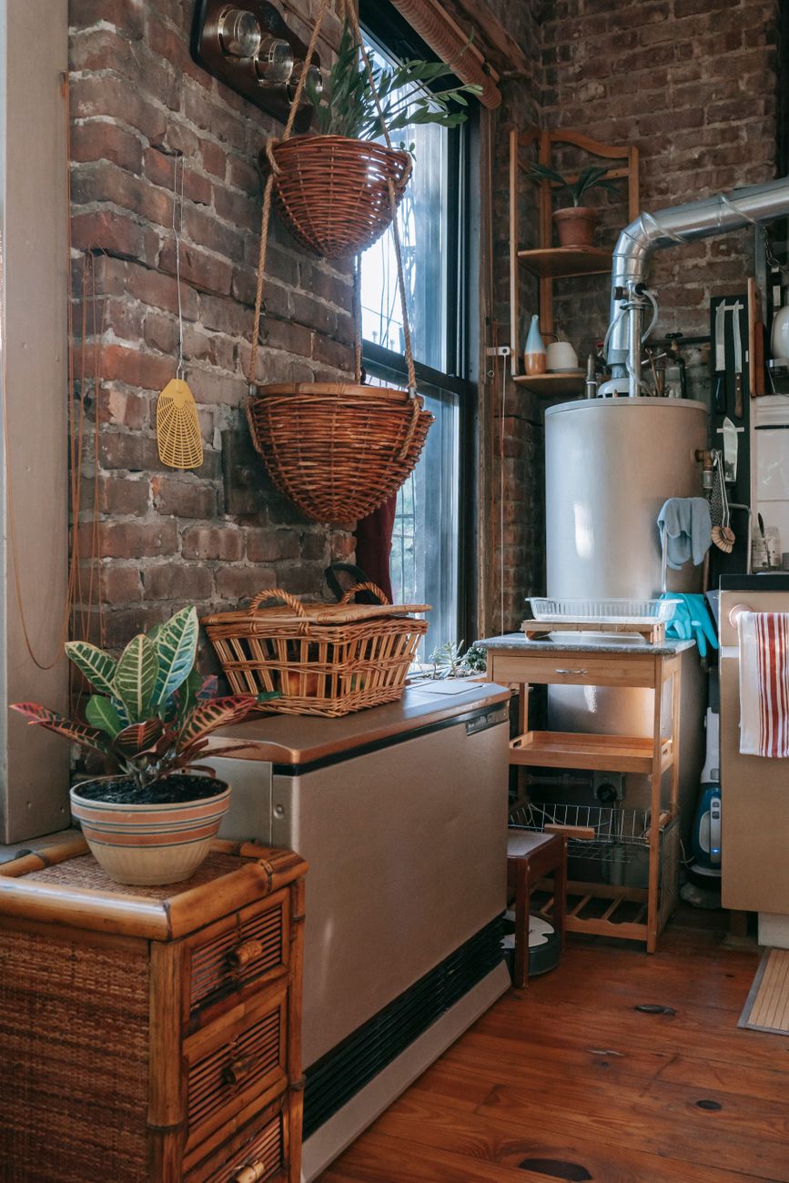 Interior design of stylish kitchen or boiler room in private cottage with shabby brick walls decorated with rustic wooden furniture and wicker baskets