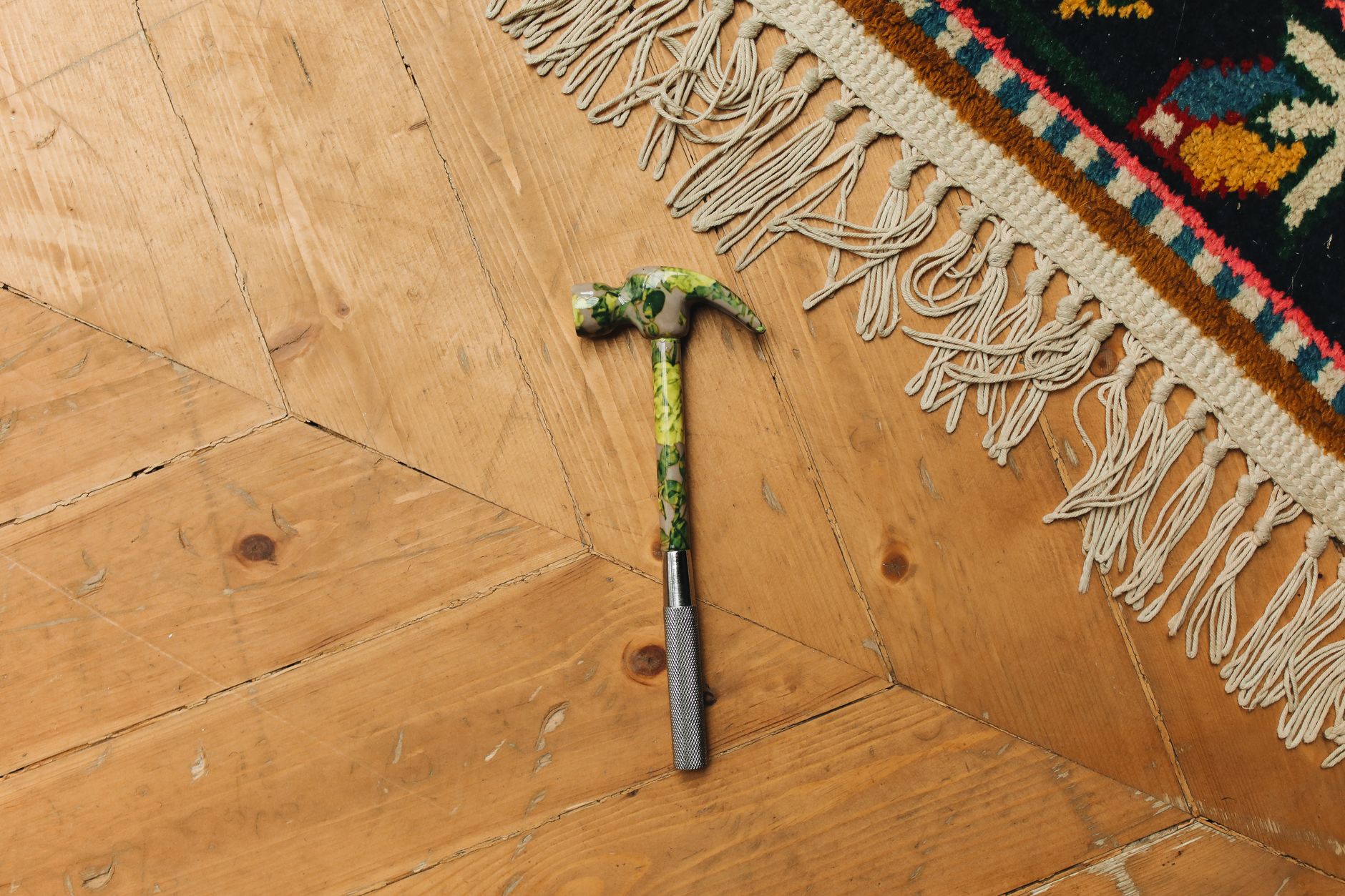 A patterned rug with a hammer on a wooden floor from a top view.