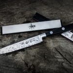 A sharp kitchen knife with water droplets on a rustic wooden surface, providing a dramatic mood.