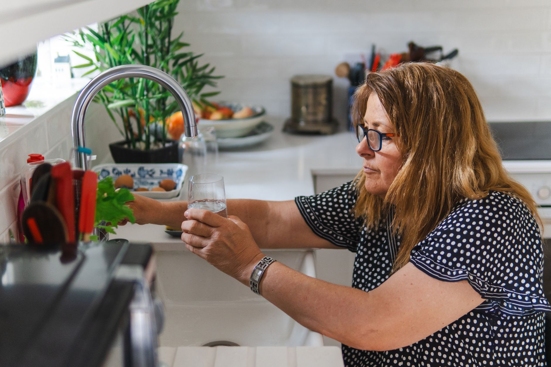 A middle aged woman filling a glass with water in a modern kitchen setting.