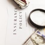 Close up image of an insurance policy with a magnifying glass, money, and toy car.
